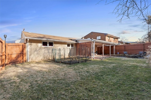 back of property featuring brick siding, a fenced backyard, a lawn, and a vegetable garden