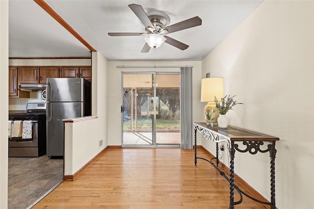 doorway with light wood-style flooring, a ceiling fan, and baseboards