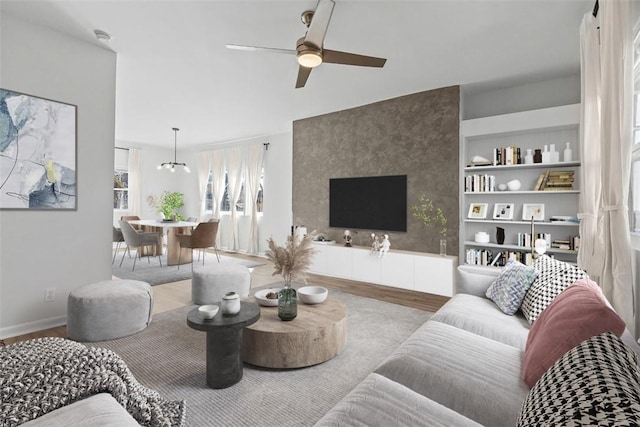 living room with a ceiling fan, built in shelves, wood finished floors, and baseboards