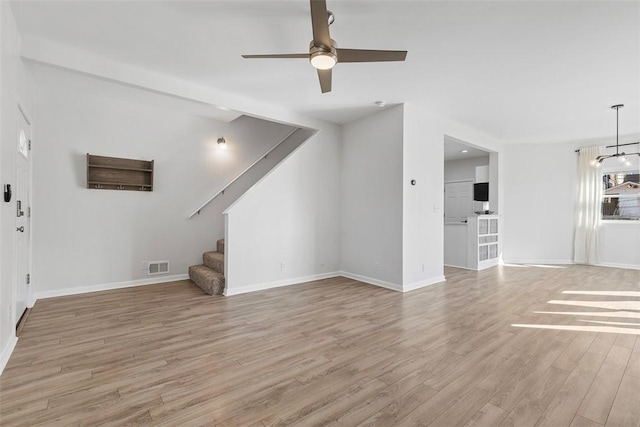 unfurnished living room featuring stairway, visible vents, baseboards, light wood-style flooring, and ceiling fan with notable chandelier