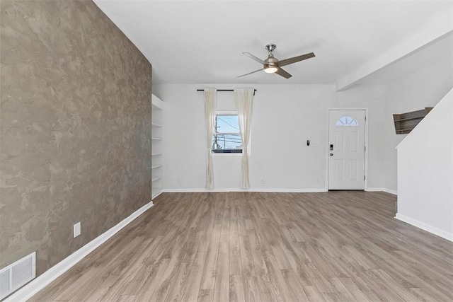 unfurnished living room featuring built in features, wood finished floors, visible vents, baseboards, and ceiling fan