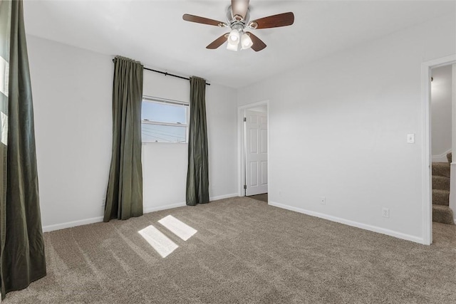 empty room featuring a ceiling fan, stairway, carpet, and baseboards