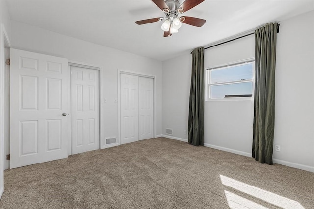 unfurnished bedroom featuring carpet, visible vents, two closets, and baseboards