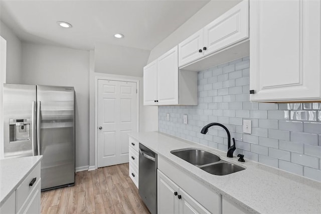 kitchen with backsplash, light wood-style flooring, appliances with stainless steel finishes, white cabinetry, and a sink