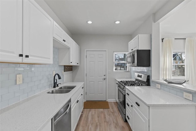 kitchen with a sink, light stone counters, white cabinetry, appliances with stainless steel finishes, and light wood finished floors