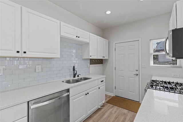 kitchen with light wood finished floors, light stone counters, white cabinets, stainless steel appliances, and a sink