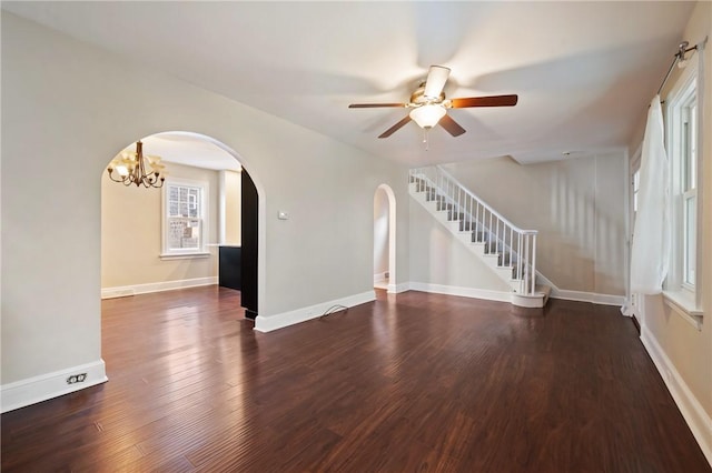 unfurnished living room featuring ceiling fan, baseboards, stairway, wood finished floors, and arched walkways