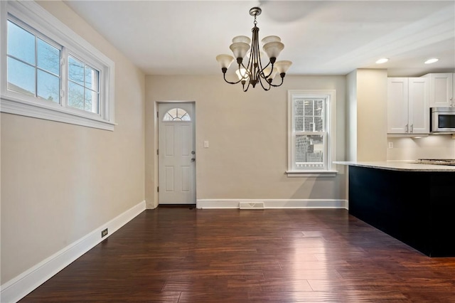 unfurnished dining area featuring a notable chandelier, baseboards, and dark wood-type flooring