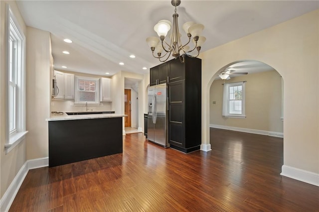 kitchen featuring dark wood-style floors, a peninsula, arched walkways, light countertops, and appliances with stainless steel finishes