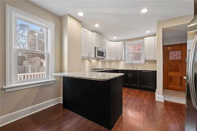 kitchen with appliances with stainless steel finishes, a peninsula, dark wood-style floors, white cabinets, and a sink