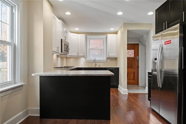 kitchen with a peninsula, a sink, dark wood-type flooring, white cabinets, and appliances with stainless steel finishes