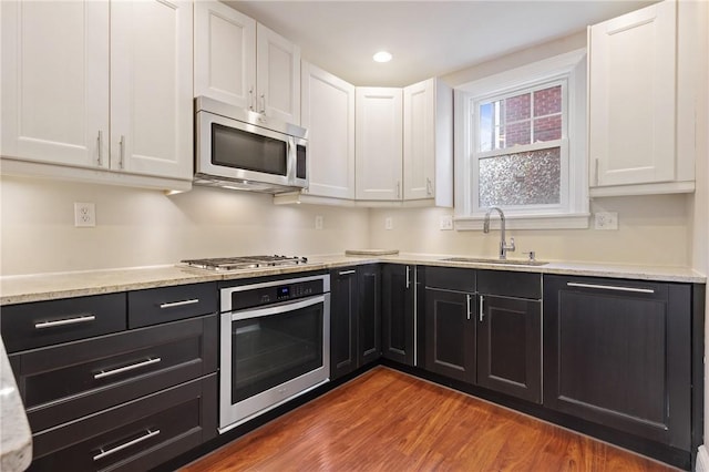 kitchen with a sink, dark cabinets, white cabinetry, and stainless steel appliances