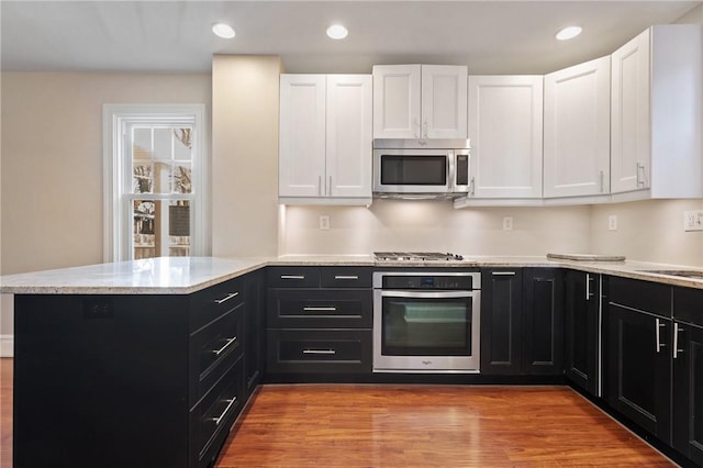 kitchen with appliances with stainless steel finishes, white cabinetry, dark cabinetry, and a peninsula