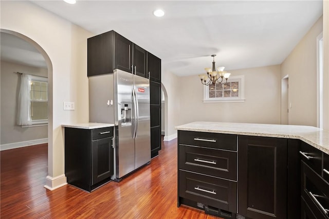 kitchen with arched walkways, dark cabinets, wood finished floors, and stainless steel fridge with ice dispenser