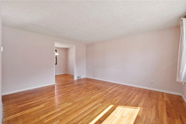 spare room featuring light wood-style flooring, baseboards, visible vents, and a textured ceiling