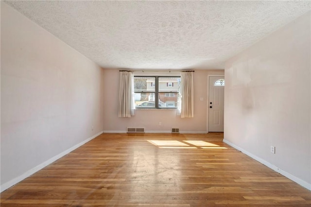 spare room with visible vents, baseboards, a textured ceiling, and wood finished floors