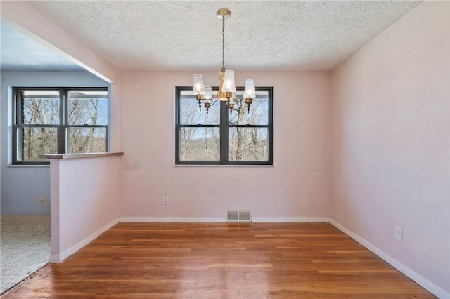 unfurnished dining area with visible vents, baseboards, wood finished floors, and a chandelier