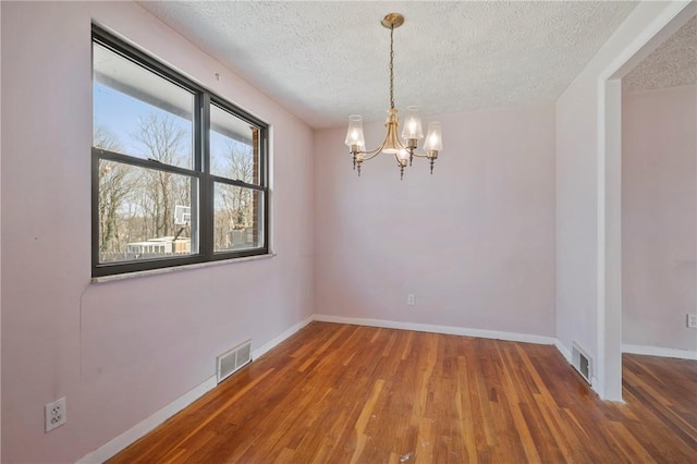 spare room featuring a textured ceiling, wood finished floors, visible vents, and baseboards