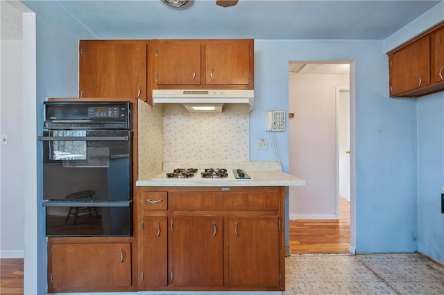 kitchen with oven, a warming drawer, under cabinet range hood, brown cabinetry, and white gas cooktop