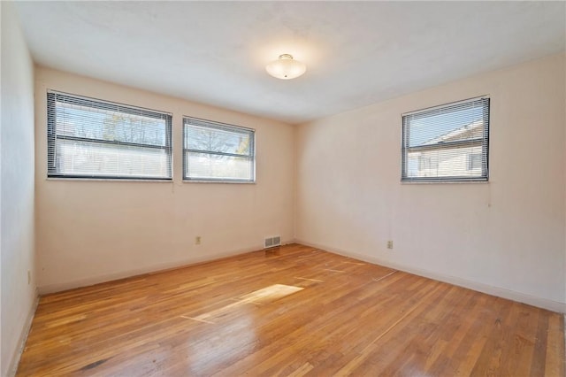 empty room with light wood-type flooring, visible vents, and baseboards