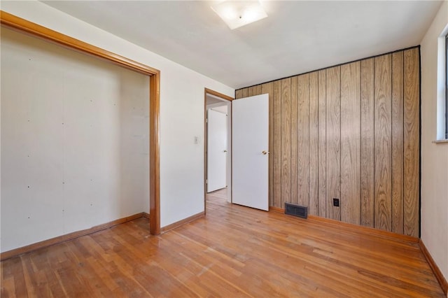 unfurnished bedroom featuring a closet, visible vents, wooden walls, and hardwood / wood-style flooring