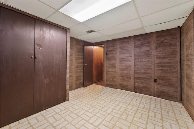 interior space featuring brick floor, a drop ceiling, visible vents, and wood walls