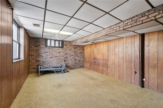 below grade area featuring visible vents, a drop ceiling, carpet floors, wooden walls, and brick wall