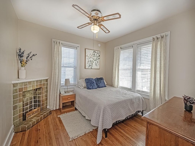 bedroom featuring ceiling fan, wood finished floors, and a tiled fireplace