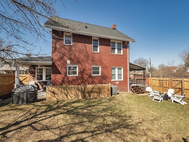 back of house with a yard, a fenced backyard, brick siding, and a chimney