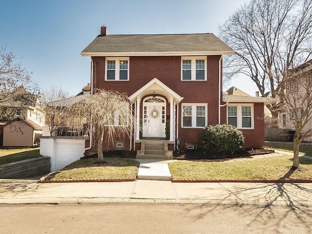 colonial inspired home with a front yard, brick siding, a chimney, and an attached garage