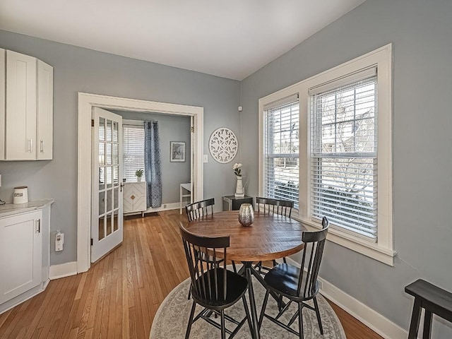 dining area featuring light wood-style flooring, a healthy amount of sunlight, baseboards, and french doors