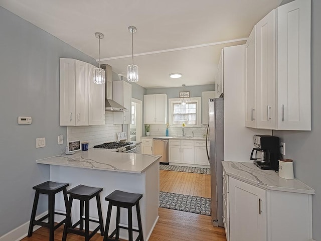 kitchen with tasteful backsplash, wall chimney range hood, appliances with stainless steel finishes, a peninsula, and a sink