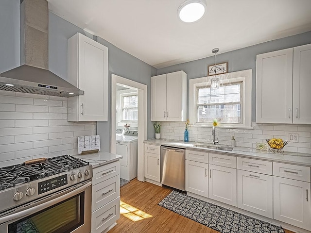 kitchen featuring independent washer and dryer, a sink, white cabinetry, stainless steel appliances, and wall chimney exhaust hood