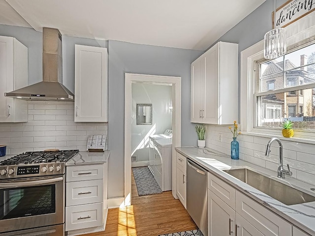 kitchen featuring white cabinets, washer and dryer, stainless steel appliances, wall chimney exhaust hood, and a sink