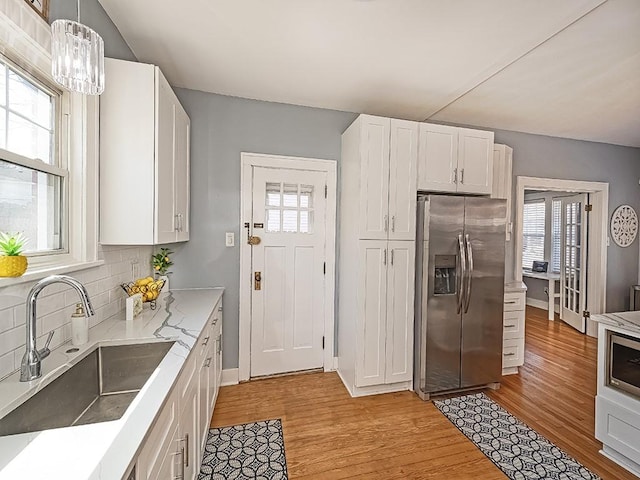 kitchen featuring white cabinets, stainless steel fridge with ice dispenser, light wood finished floors, and a sink