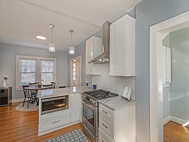 kitchen with stainless steel appliances, light wood finished floors, white cabinets, and wall chimney range hood