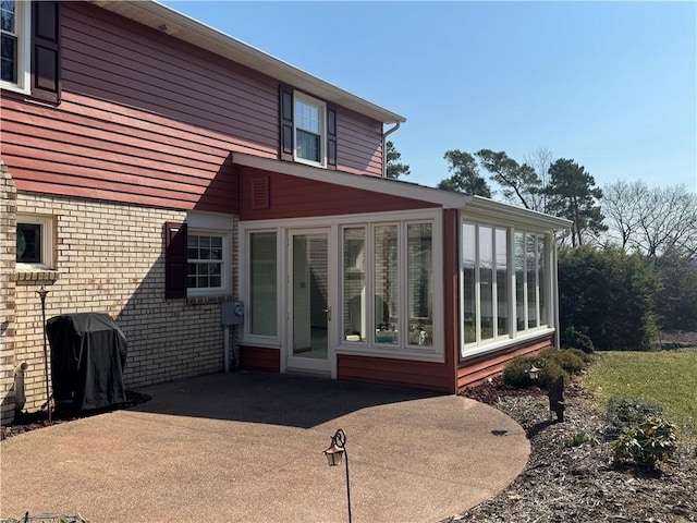 rear view of house featuring a patio area, brick siding, and a sunroom