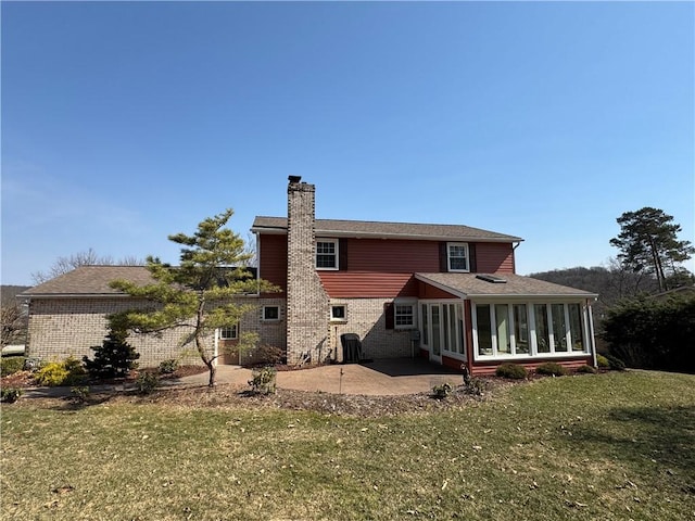 back of property with a patio, a yard, a sunroom, a chimney, and brick siding