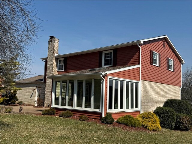 back of house with a yard, brick siding, a sunroom, and a chimney