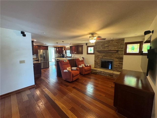 unfurnished living room featuring a textured ceiling, dark wood-style floors, a fireplace, baseboards, and ceiling fan