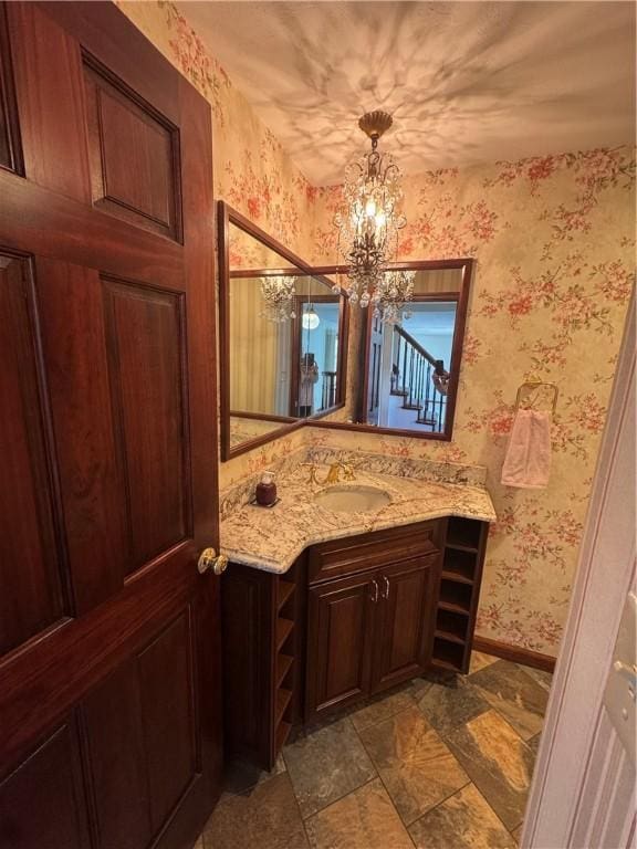 bathroom with a notable chandelier, wallpapered walls, vanity, and baseboards