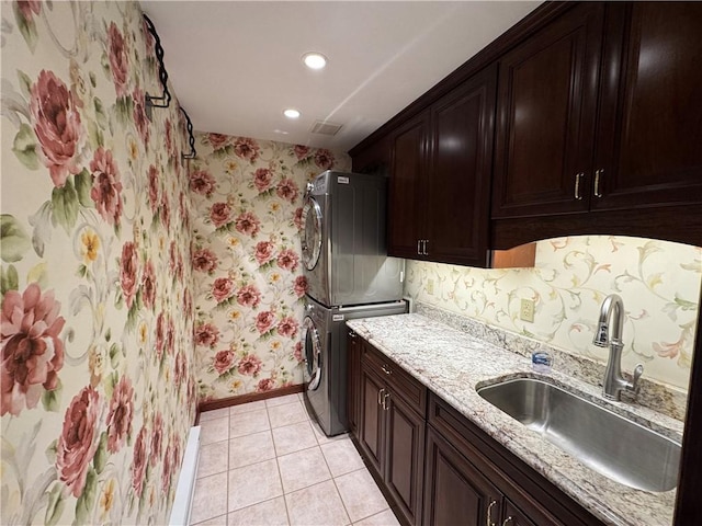 kitchen featuring a sink, light tile patterned flooring, stacked washer / dryer, baseboards, and light stone countertops