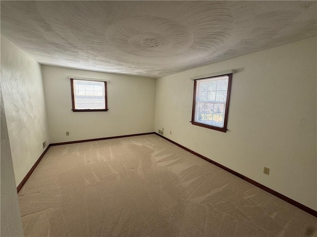 spare room with light colored carpet, a textured ceiling, and baseboards