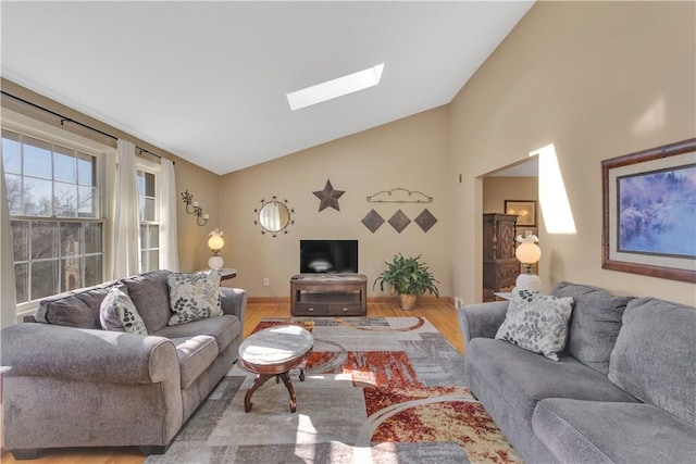 living room featuring baseboards, vaulted ceiling with skylight, and wood finished floors