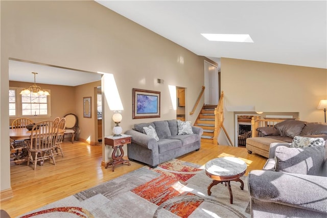 living area with stairway, visible vents, vaulted ceiling, a notable chandelier, and light wood-type flooring