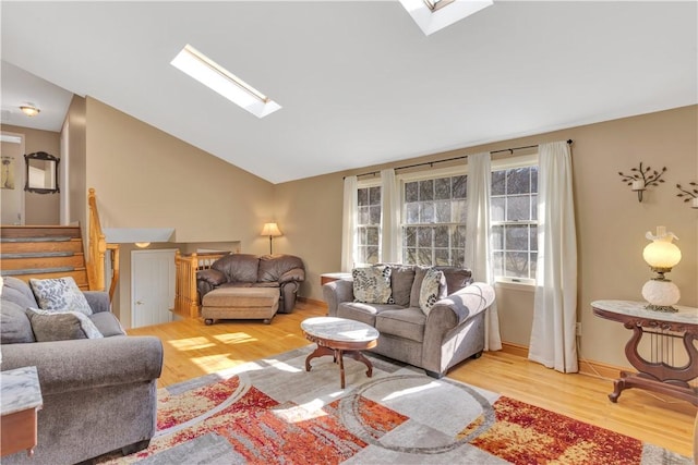 living area featuring stairway, vaulted ceiling with skylight, baseboards, and wood finished floors