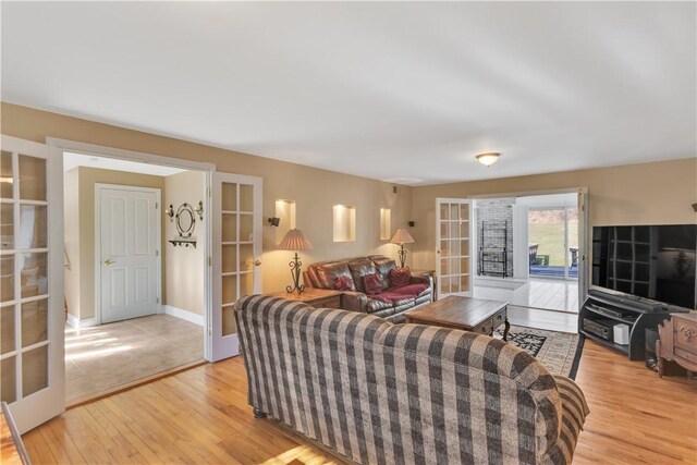 living area featuring french doors, baseboards, and light wood finished floors