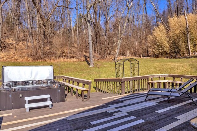 wooden terrace with a lawn, a hot tub, and a view of trees