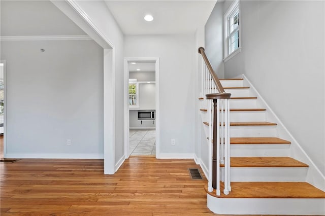 staircase featuring visible vents, a healthy amount of sunlight, baseboards, and wood finished floors