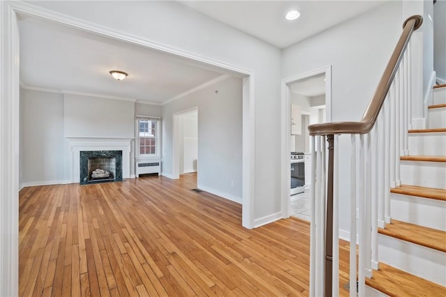 unfurnished living room featuring a high end fireplace, crown molding, radiator heating unit, and light wood-style floors